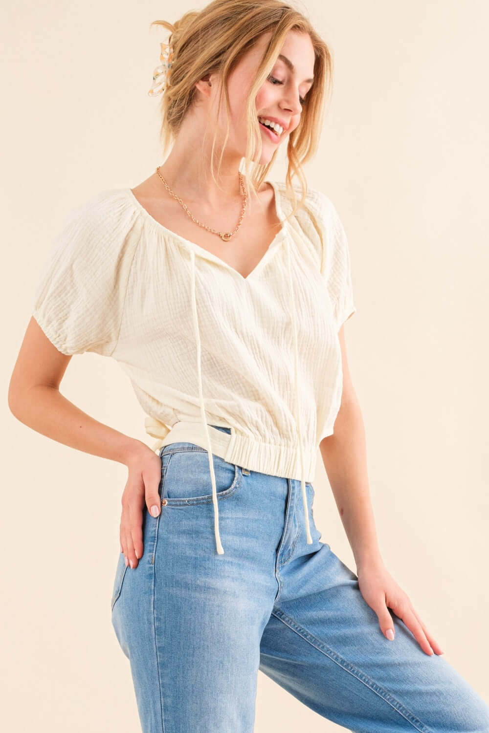 Woman wearing the Back Waist Tie Cropped Blouse with a stylish back tie detail, paired with high-waisted jeans for a trendy look.