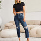 Woman wearing Crop Dylan Full Size Tummy Control Distressed High Waist Raw Hem Jeans from RFM Jeans, styled with a black crop top and sandals.