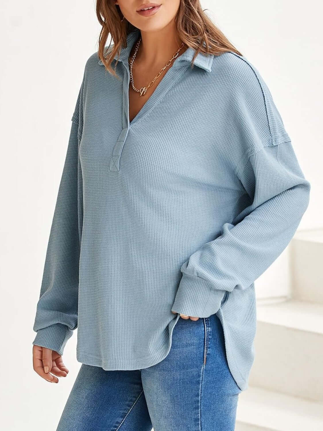 Woman wearing light blue waffle-knit long sleeve sweatshirt with johnny collar, paired with blue jeans.