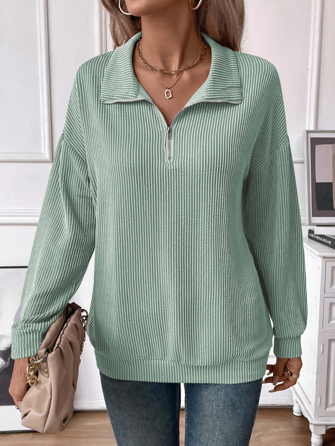 Woman wearing a green striped half zip long sleeve t-shirt with slightly stretchy material, paired with blue jeans and accessorized with a beige handbag.