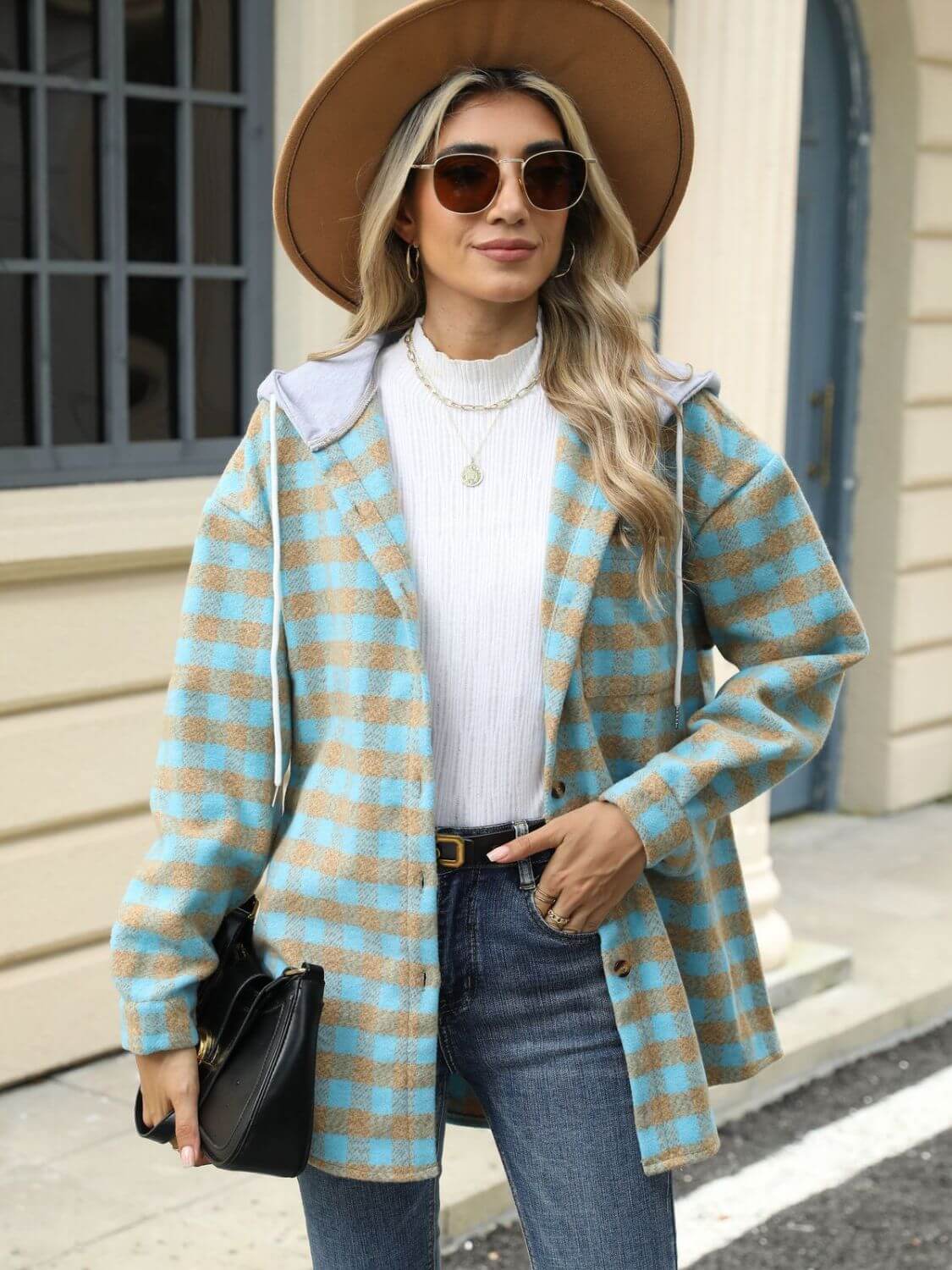 Woman wearing a Bella Road Drawstring Plaid Long Sleeve Hooded Jacket in blue and beige, accessorized with a hat, sunglasses, and a black purse.