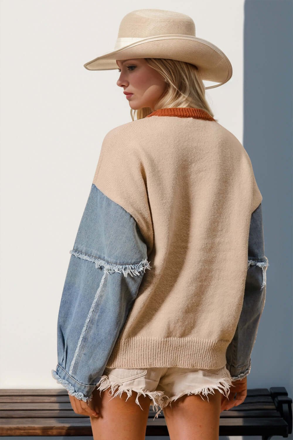 Woman wearing raw edge sweater with star pattern, beige and denim sleeves, paired with frayed shorts and cowboy hat. Casual chic style.