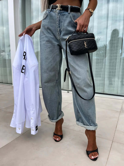 Woman wearing high waist wide leg jeans with a black belt, holding a white shirt and a black crossbody bag, perfect for stylish outfits.