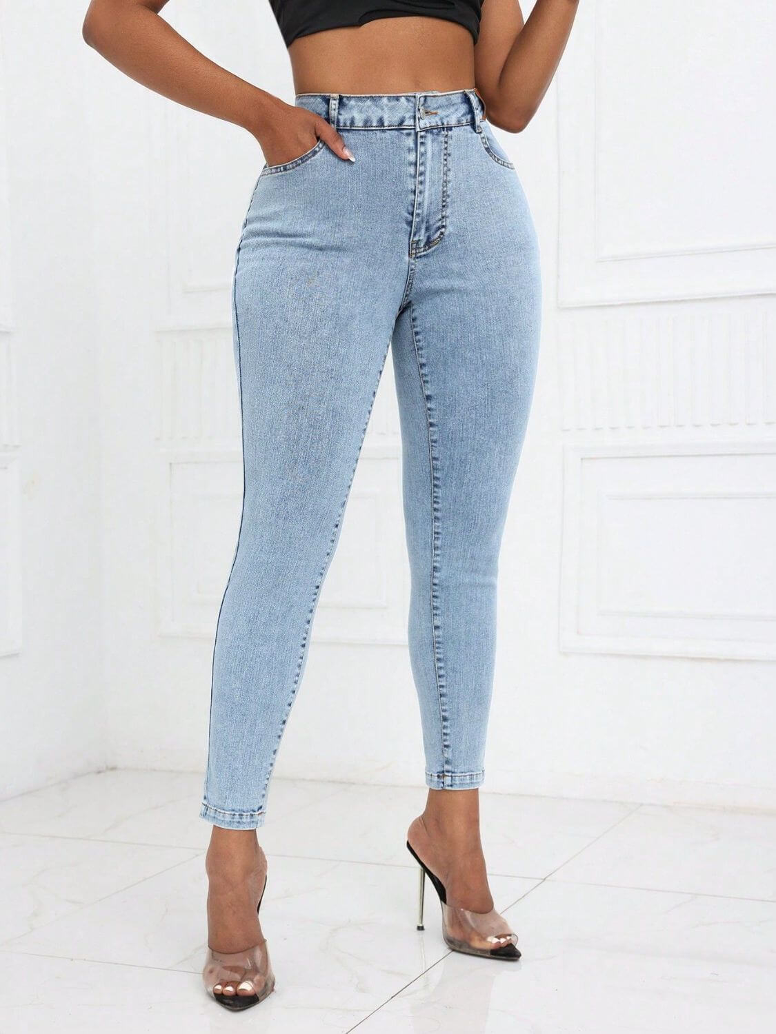 Woman wearing Bella Road High Waist Skinny Jeans with pockets, light-wash, showing front view with paired clear high heels.