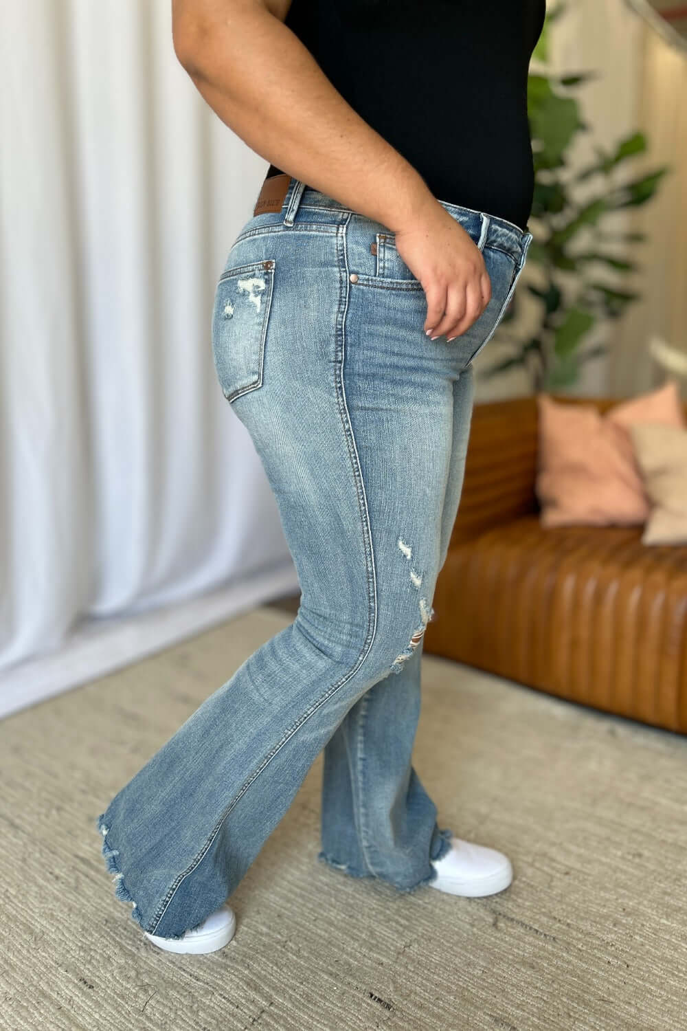 Woman wearing Judy Blue medium rise tummy control destroy flare jeans with distressed detailing, side view.