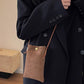 Woman holding Bella Road Suede Snap Down Crossbody Bag, mini size, brown color with snap closure and crossbody strap, styled with black coat