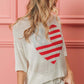 Woman wearing a white striped heart contrast knit top with red stripes on a heart design and white shorts against a pink background