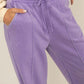 Woman wearing purple drawstring high rise wide leg pants showing pockets and waist detail.