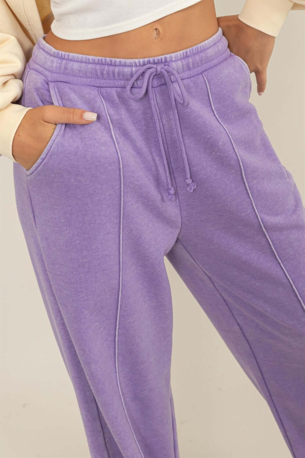 Woman wearing purple drawstring high rise wide leg pants showing pockets and waist detail.