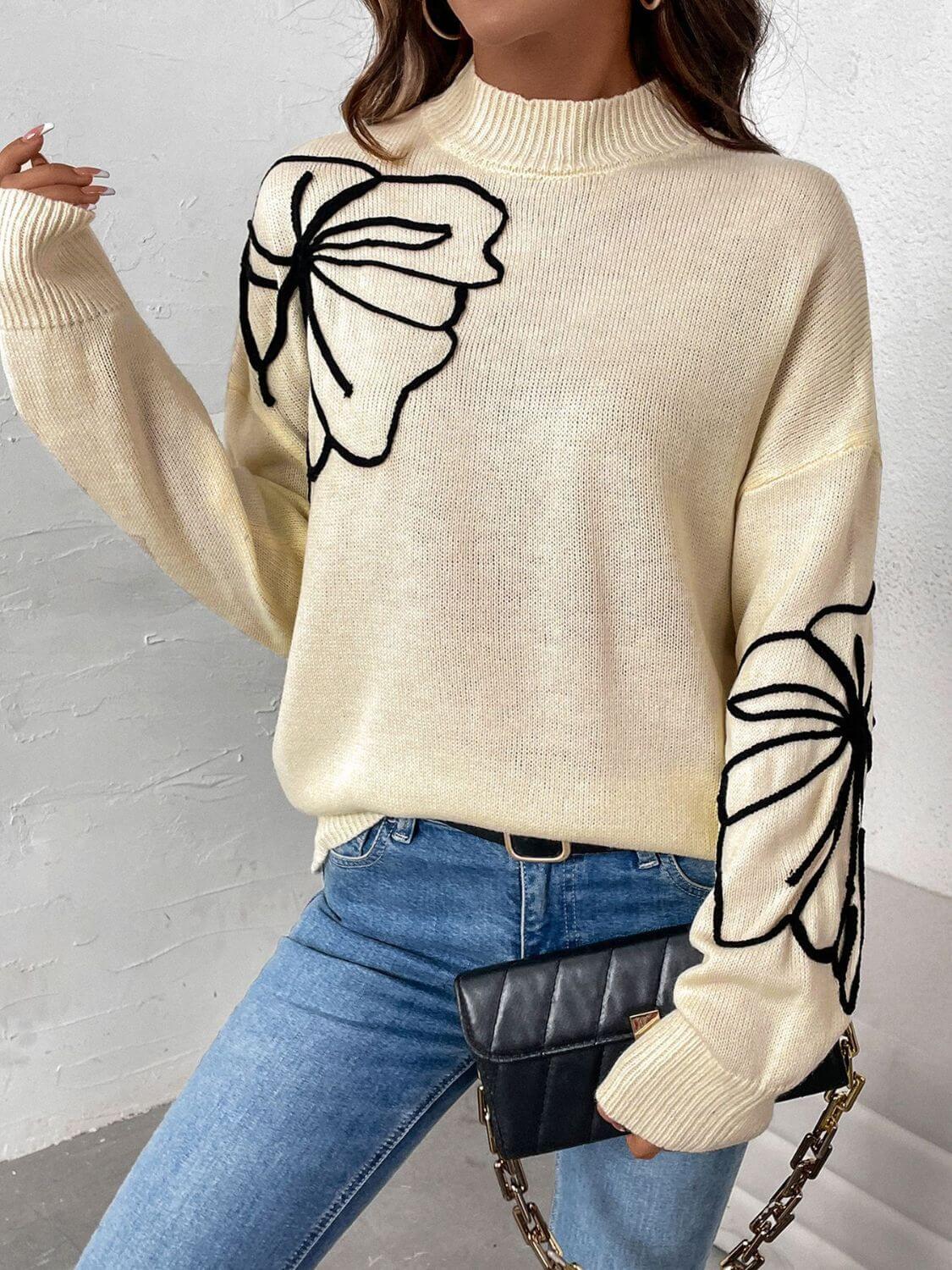 Woman wearing Perfee Mock Neck Dropped Shoulder Long Sleeve Sweater with floral design, paired with blue jeans and black clutch