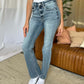 Woman wearing Judy Blue Full Size Medium Rise Bootcut Jeans with white top, standing in stylish living room.