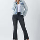 Woman wearing a stylish button-up washed denim jacket by Risen Jeans with black distressed pants and a white top.