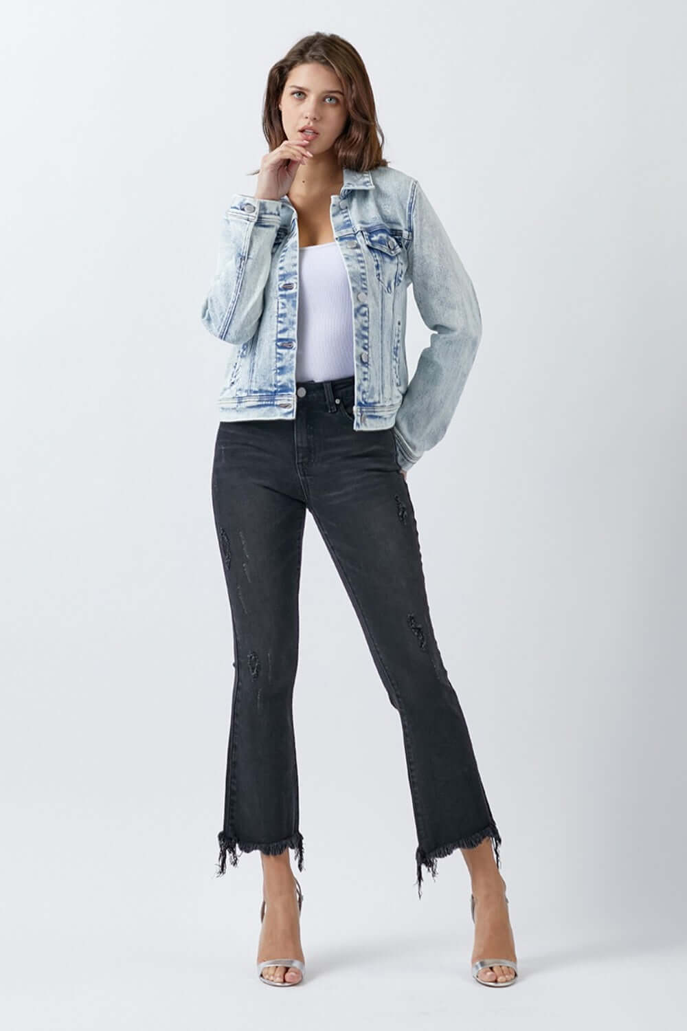 Woman wearing a stylish button-up washed denim jacket by Risen Jeans with black distressed pants and a white top.