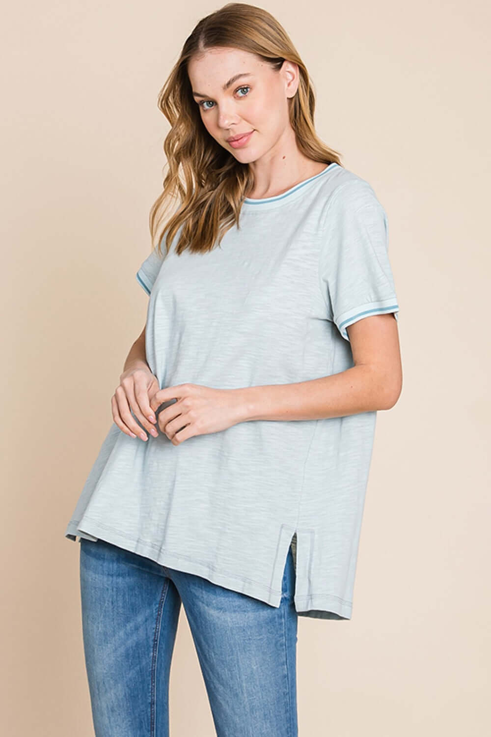 Woman wearing a light gray contrast trim short sleeve slit T-shirt paired with blue jeans, showcasing modern, stylish, and relaxed fit design