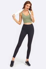 Model showcasing the Millennia Deep V-Neck Crop Sports Bra in olive green with black leggings, perfect for workouts.