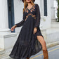 Woman wearing Bella Road black embroidered V-neck dress with sheer sleeves and ruffled hem, styled with a brown hat and boots.