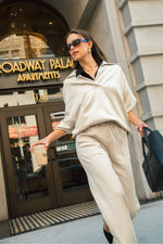 Stylish woman in a Johnny Collar Dropped Shoulder Sweatshirt and wide pants, sipping coffee outside Broadway Palace Apartments.