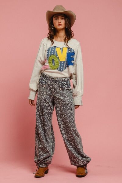 Model wearing BiBi LOVE Heart Patch Slit Sweatshirt with floral pants and cowboy hat, exuding casual style.