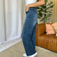 Woman wearing RFM Full Size High Rise Tummy Control Wide Leg Jeans with white top standing indoors