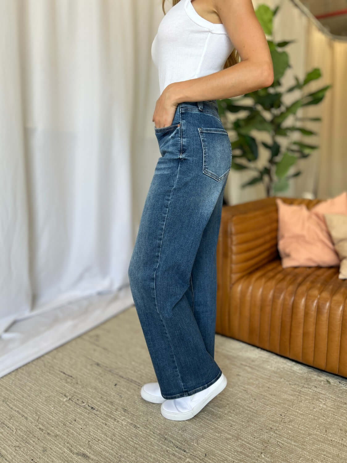 Woman wearing RFM Full Size High Rise Tummy Control Wide Leg Jeans with white top standing indoors