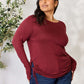 Curve model wearing drawstring round neck long sleeve top in burgundy, paired with blue jeans, standing near a plant.