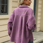 Woman wearing a Bella Road plaid collared neck long sleeve jacket in purple, standing outdoors by a cream-colored building