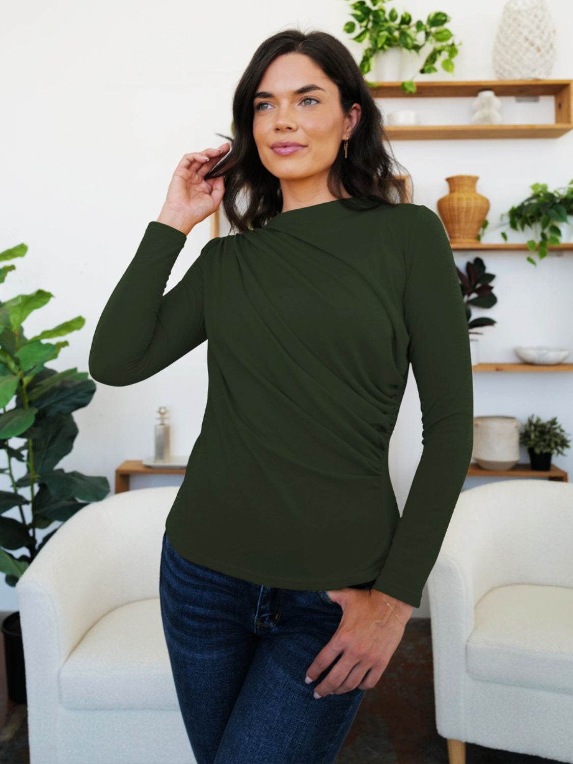 Woman wearing Army Green ruched mock neck long sleeve t-shirt, perfect for fall layering and style, standing in a cozy living room.