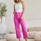 Woman wearing bright pink high waist jeans with raw hem and white tank top, standing in modern living room.