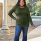 Plus-size model wearing green round neck long sleeve t-shirt, standing outdoors in a casual setting.