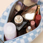 Stylish checkered knitted cosmetic pouch filled with makeup, brushes, and beauty essentials in pastel colors.