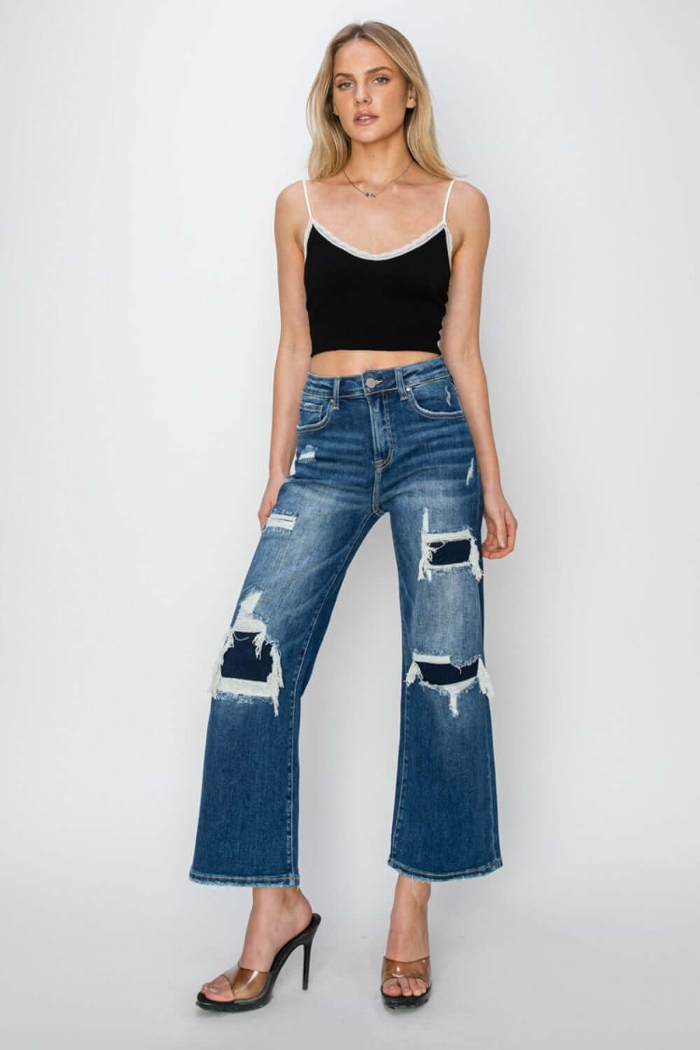 Model wearing Risen Jeans high rise patch detailed wide leg crop jeans with a black crop top and high heels.