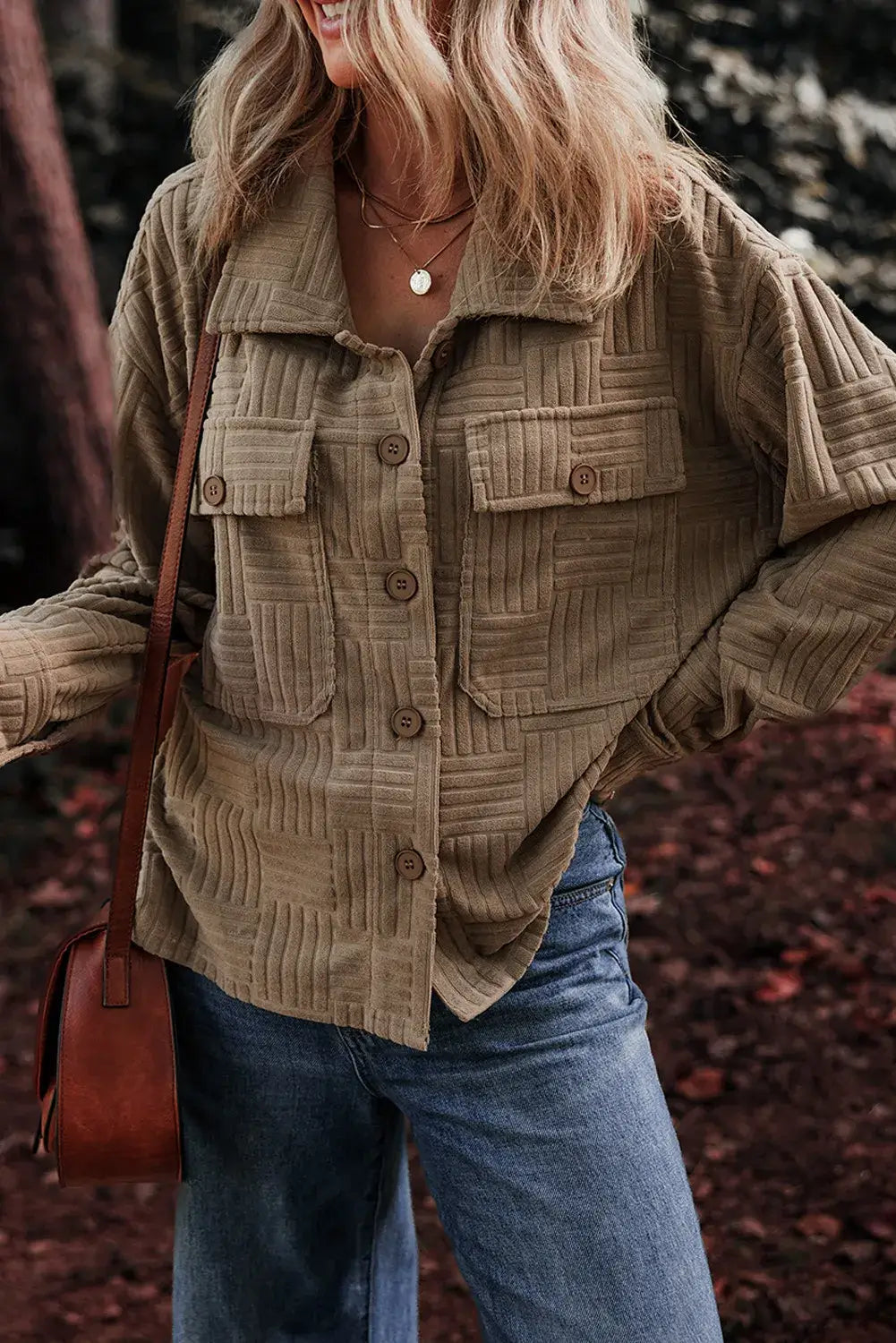 Woman wearing a textured pocketed collared neck long sleeve shacket with brown buttons, styled with blue jeans and a brown shoulder bag.