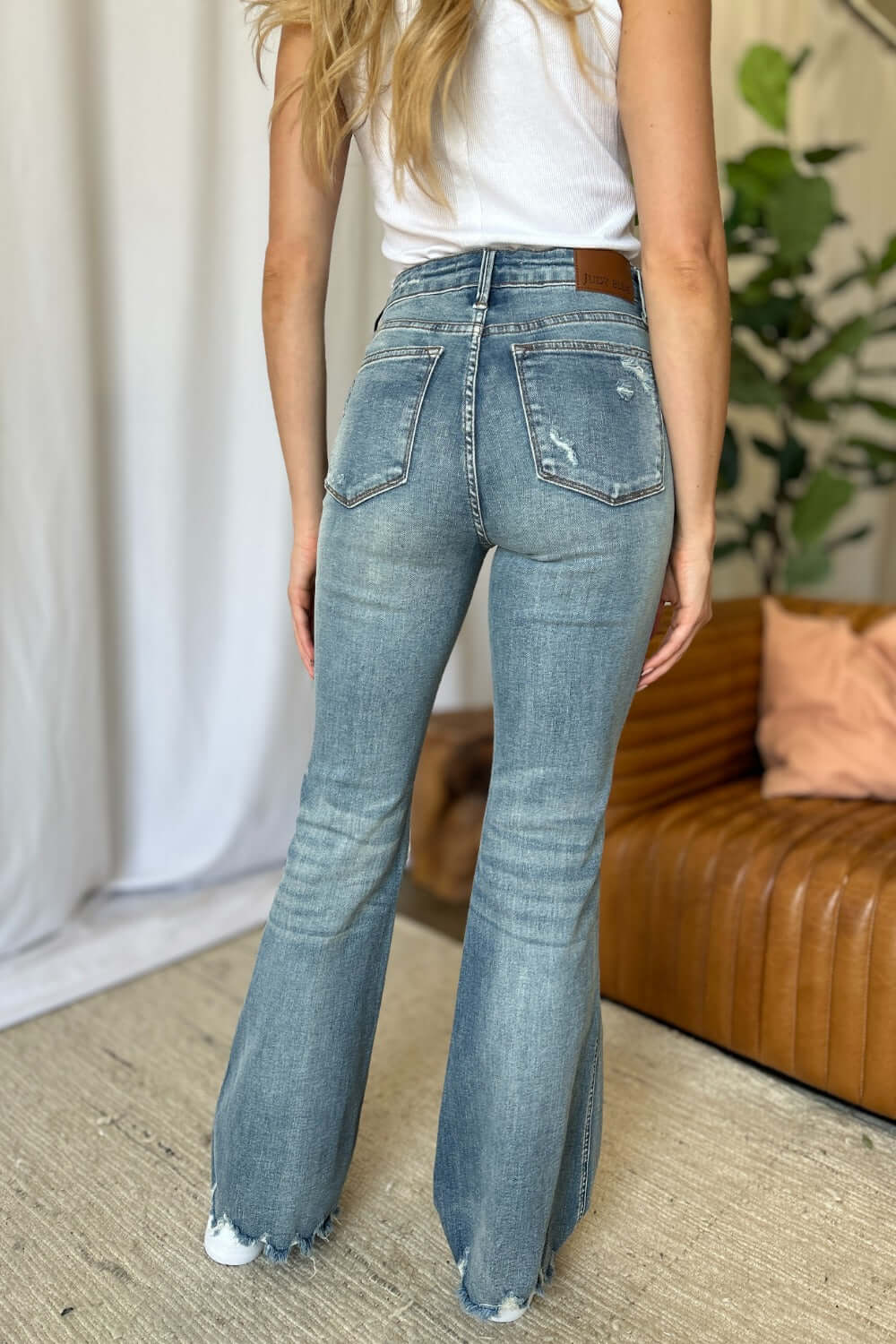 Woman wearing Judy Blue medium rise tummy control destroy flare jeans, showcasing back view, with distressed details and flattering fit.