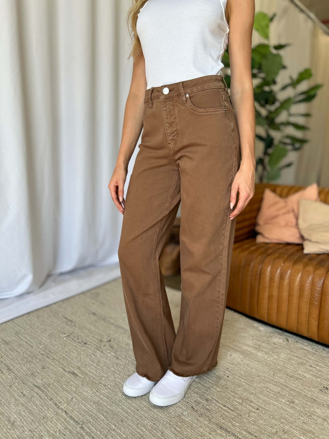 Woman wearing RFM Full Size High Rise Garment Dye Wide Leg Jeans in brown, styled casually with a white tank top and white sneakers.