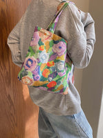 Woman holding a medium-sized printed canvas handbag with zipper, featuring colorful floral design.