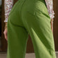 Woman wearing green wide leg jeans with pockets, shown from the back, paired with a floral top.