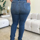 Woman wearing High Waist Distressed Skinny Jeans by Judy Blue, showcasing back pockets and flattering fit, standing in modern living room.