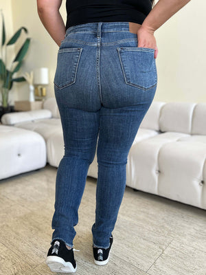 Woman wearing High Waist Distressed Skinny Jeans by Judy Blue, showcasing back pockets and flattering fit, standing in modern living room.