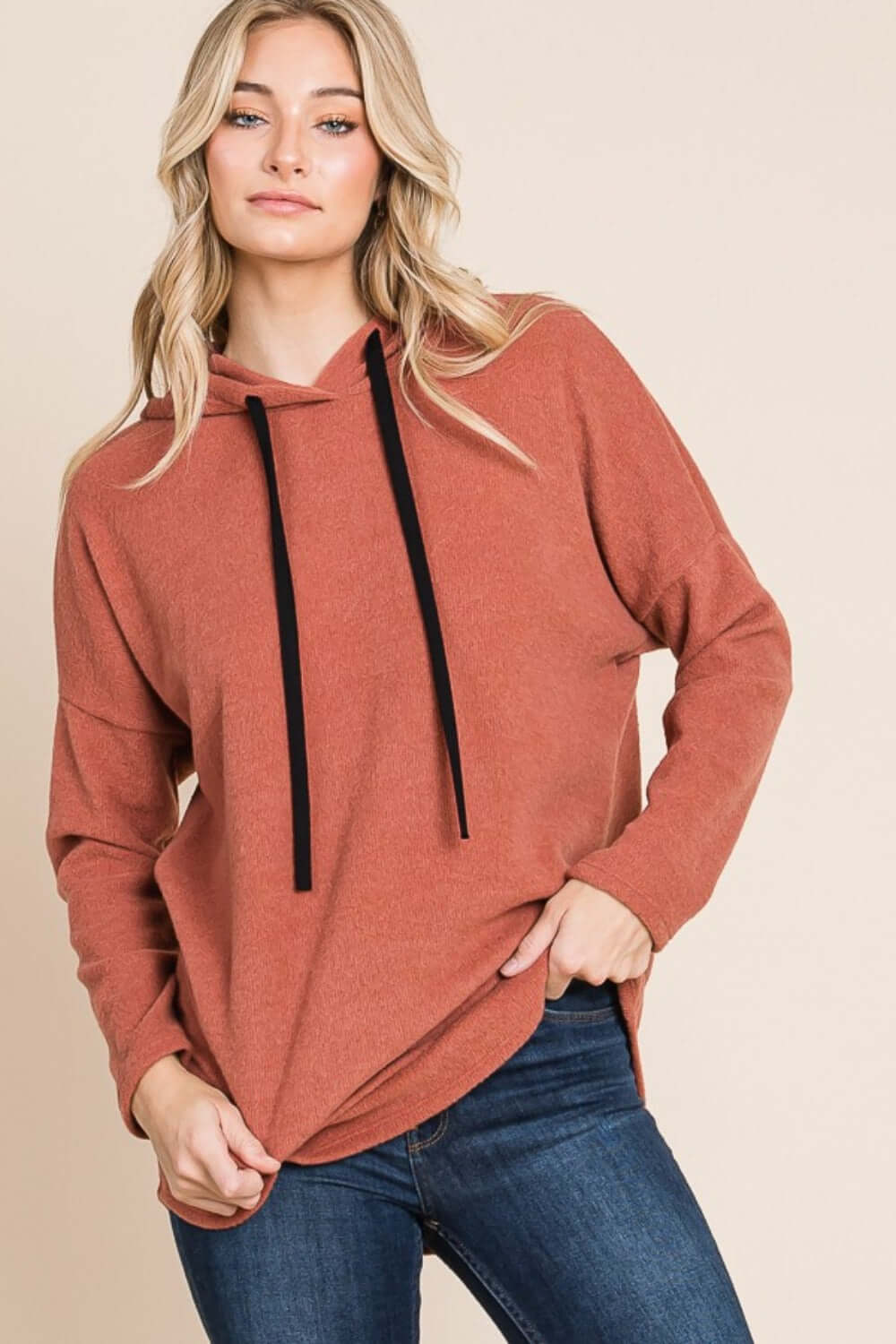 Woman wearing cozy BOMBOM contrast drawstring drop shoulder knit hoodie in rust color, paired with jeans for a casual look.