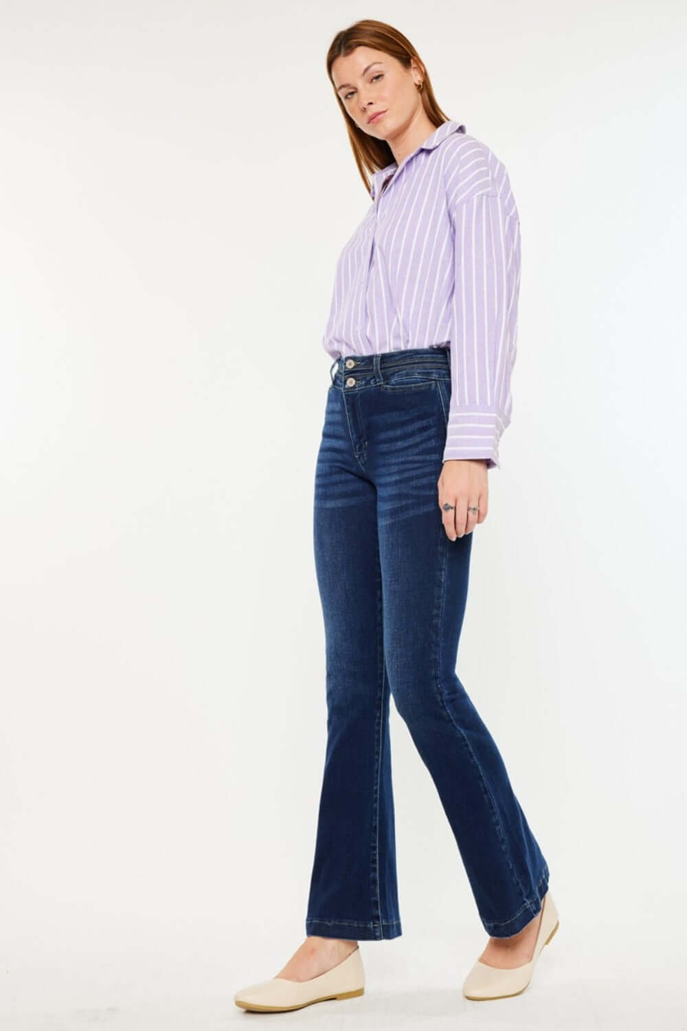 Woman wearing Kancan high-rise double waistband flare jeans in dark wash, paired with a striped blouse and flats.