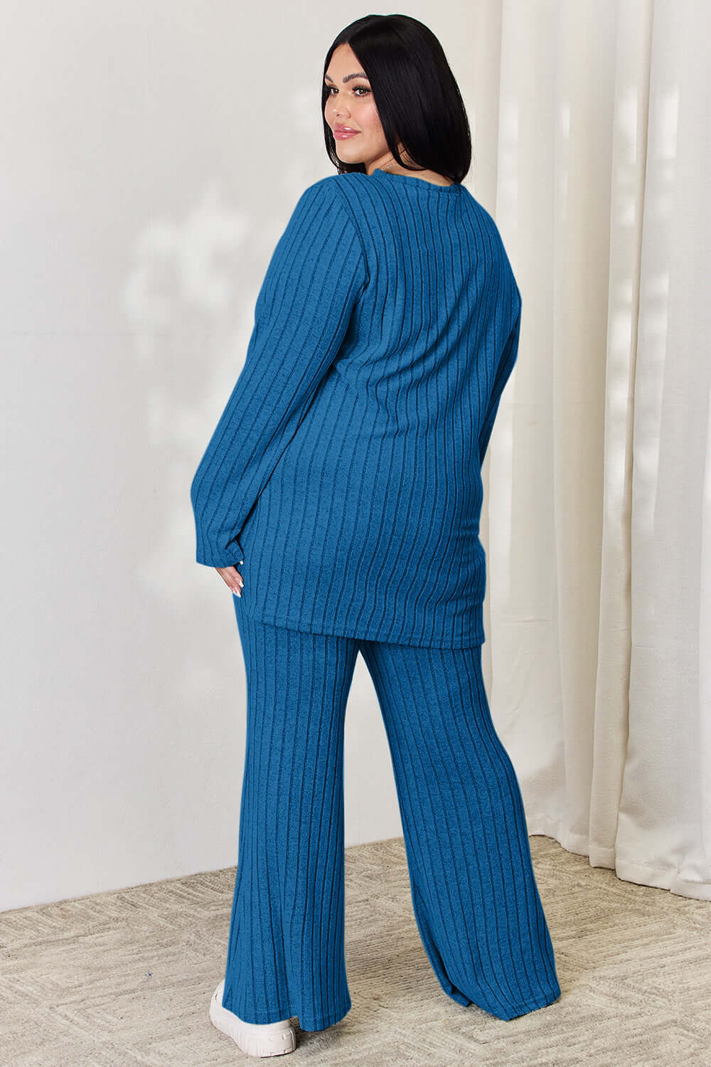 Plus-size model wearing blue ribbed high-low top and wide leg pants set, showing back view.