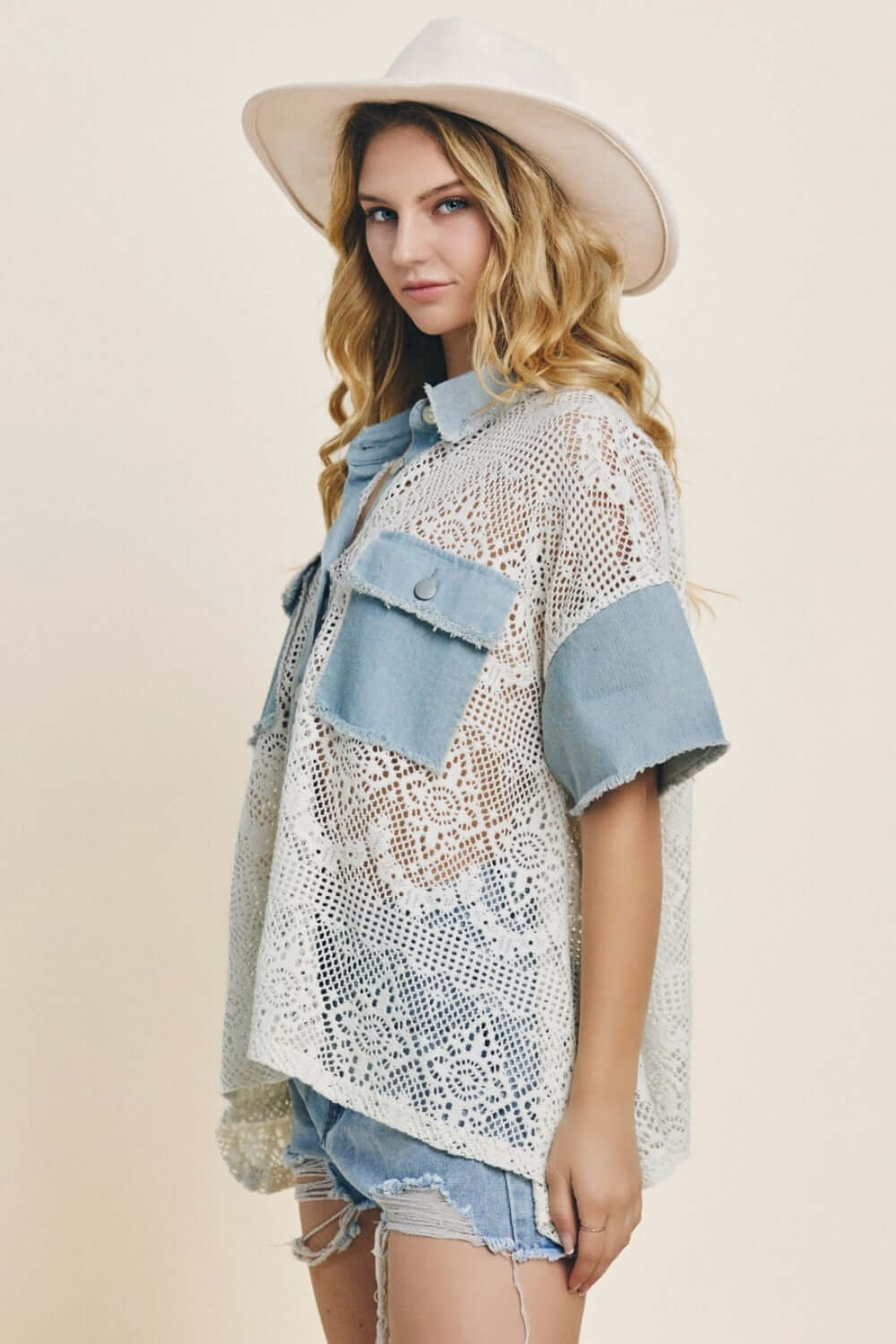 Woman wearing Button Up Short Sleeve Lace Shirt with denim accents, paired with a stylish white hat and distressed denim shorts.