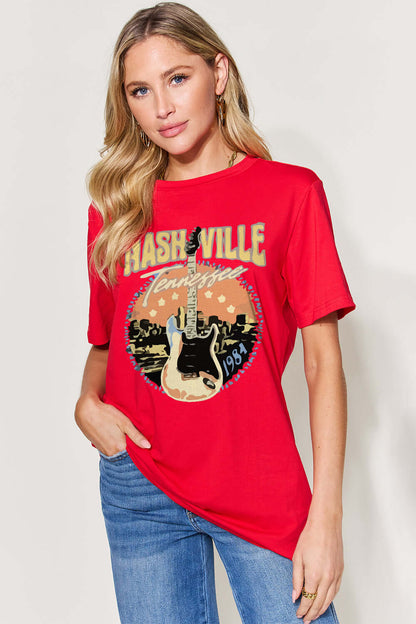 Woman wearing red graphic round neck short sleeve T-shirt with Nashville Tennessee guitar design, paired with blue jeans.