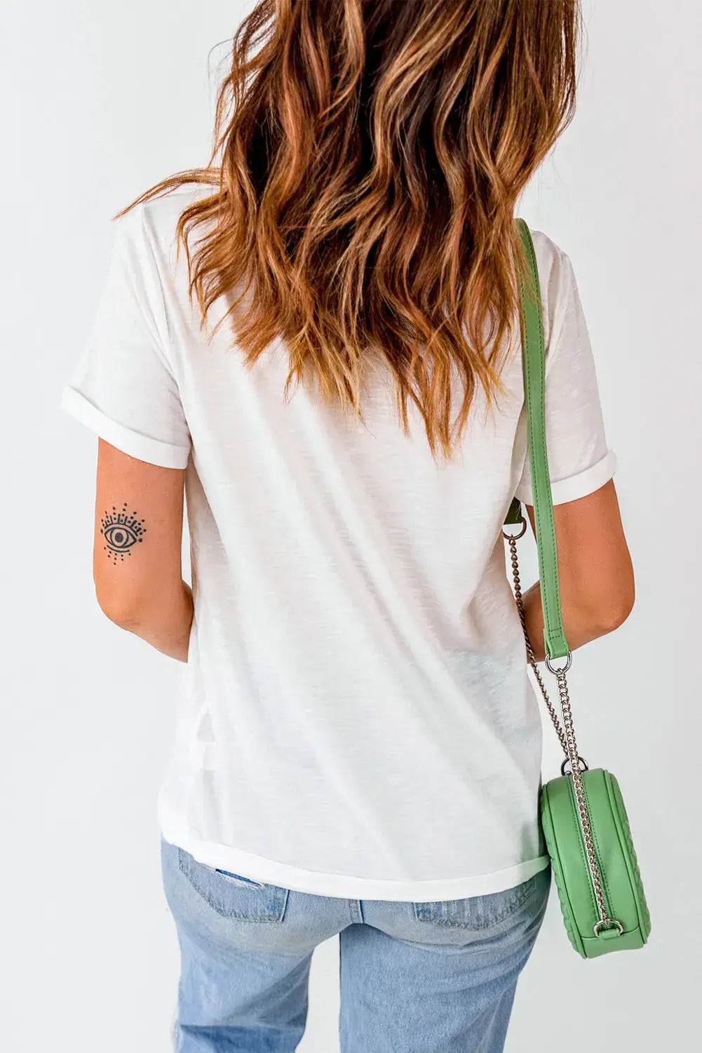 Woman wearing a white GAME DAY round neck short sleeve t-shirt with slightly stretchy fabric, blue jeans, and green purse from the back.