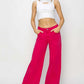 Woman wearing high rise wide leg jeans in vibrant pink with a white crop top and white sneakers, showcasing Risen Jeans style.