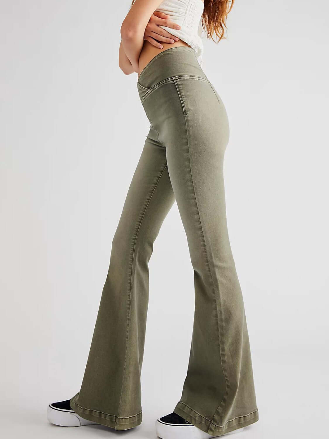 Woman wearing asymmetric waist flare jeans in green featuring a unique design, standing confidently in a side pose.