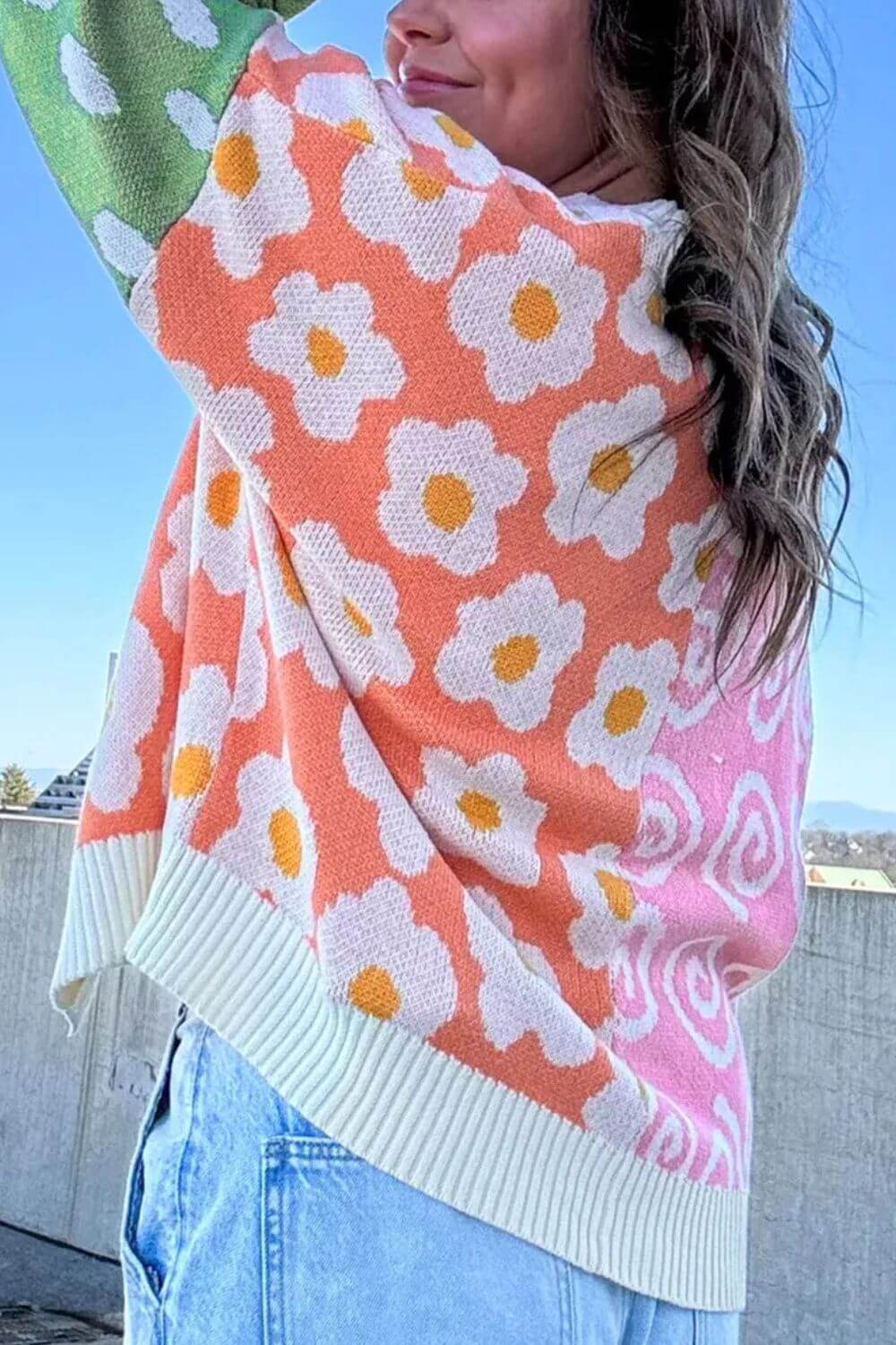 Woman wearing a vibrant color block open front long sleeve cardigan with floral patterns, white trim, and light blue jeans.