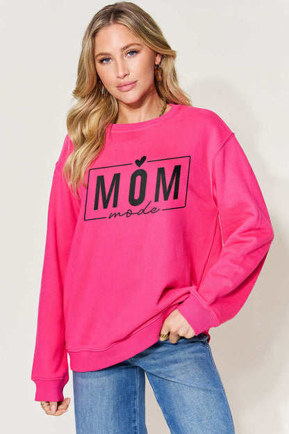 Woman wearing a pink "Mom Mode" letter graphic long sleeve sweatshirt, paired with blue jeans.