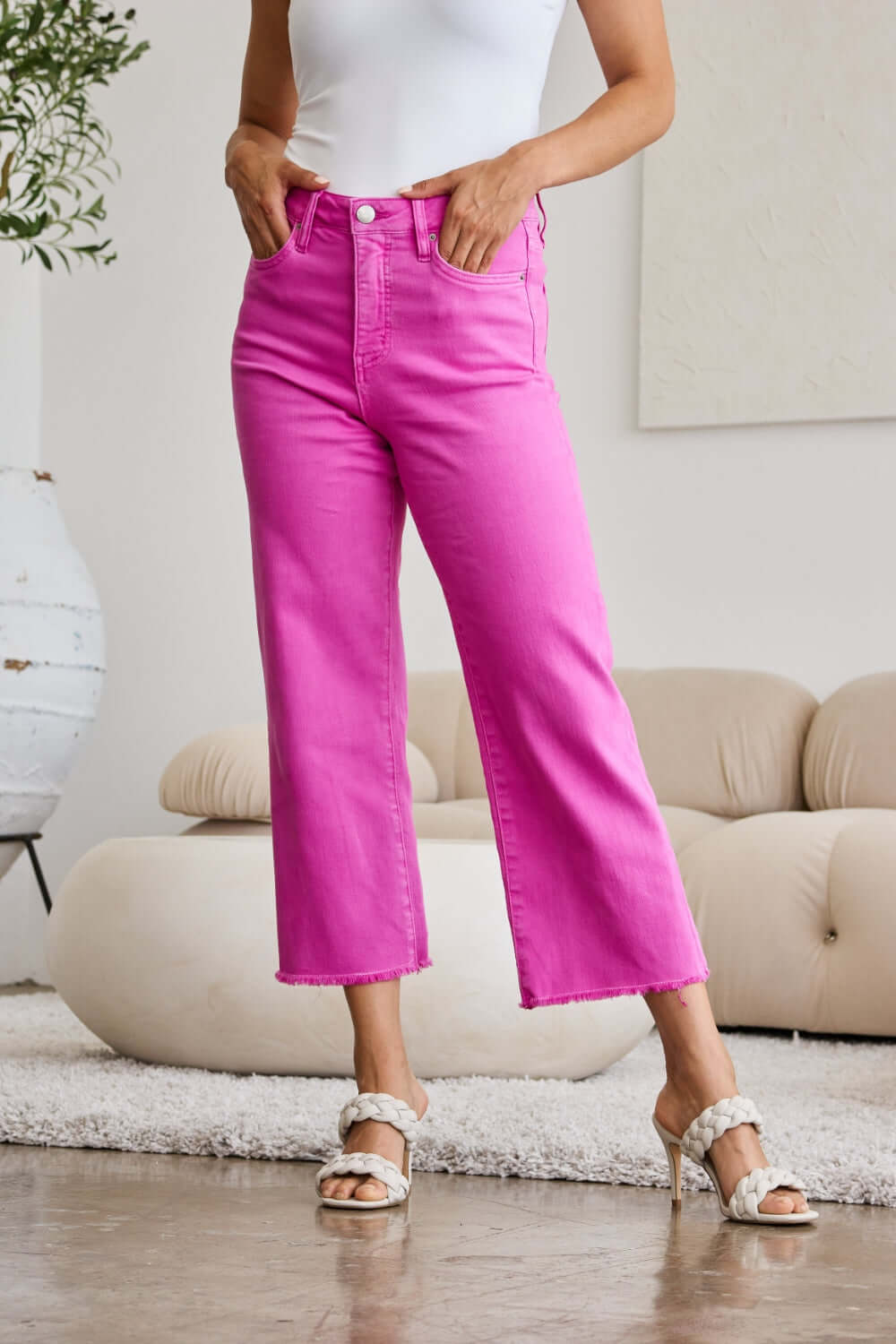 Woman wearing RFM Jeans' Crop Chloe Full Size Tummy Control High Waist Raw Hem Jeans in pink, paired with heels.