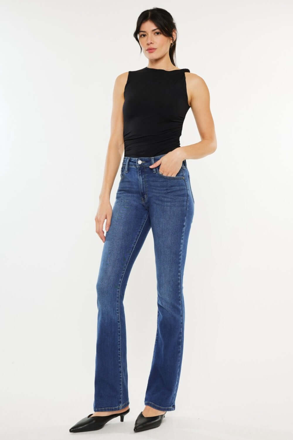 Woman wearing Kancan High Rise Slim Bootcut Jeans in medium stone wash with black top and heels, showcasing a stylish look.